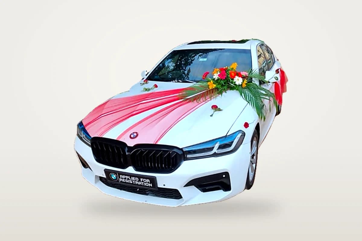 White BMW 5 Series decorated with red ribbon and flowers for a wedding